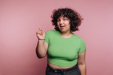 Young person in a green shirt poses playfully against a pink background in a studio setting