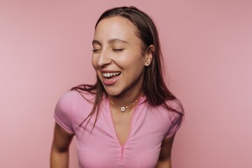 Woman smiles joyfully in a bright pink setting, showcasing happiness and playful energy during a casual moment
