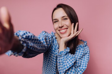 Woman smiling and posing playfully against a pink background in a checkered blouse