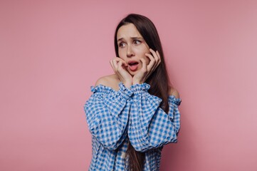 Woman expressing surprise with long hair, wearing a blue checked shirt against a pink background during a studio photoshoot