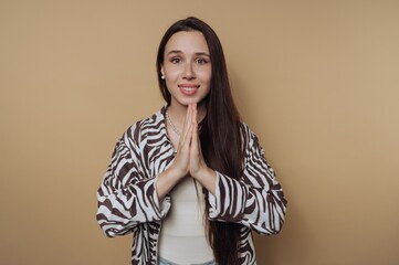 Woman with long hair wearing a zebra print jacket poses with hands together in front of a plain background
