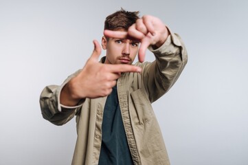 Young man creates a frame with his hands while posing against a plain backdrop during a studio photo session