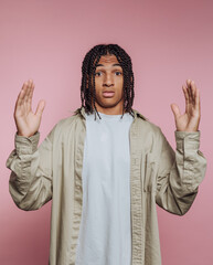 Young man with braided hair holds hands up against a pink wall during a casual portrait session in a studio environment