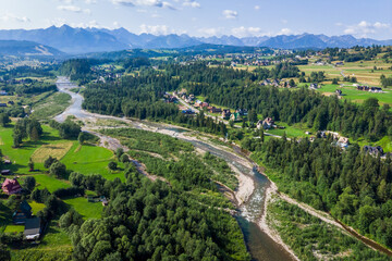 Obraz premium Wide aerial drone view of the Tatra Mountains and Białka Tatrzańska village. The braided Białka River flows through the valley, surrounded by green fields in July.