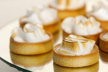 Small lemon meringue tartlets displayed on a reflective tray at a catered event, showcasing fresh pastries prepared for a formal gathering.