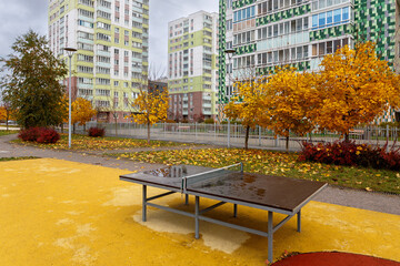 A wet ping pong table tennis table stands on a sports ground in the autumn courtyard of a residential complex.
