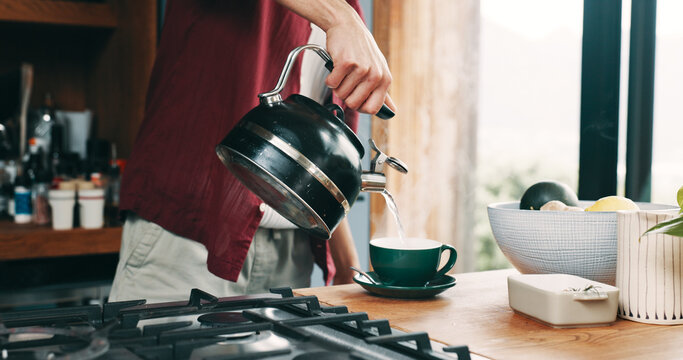 Hand, pouring tea and steam with person in kitchen of home for beverage preparation at counter. Boiling water, cup and kettle with man closeup in apartment for drink, me time routine or wellness