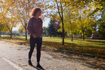 A middle-aged woman with a backpack on her back walks through the park on a sunny autumn day.