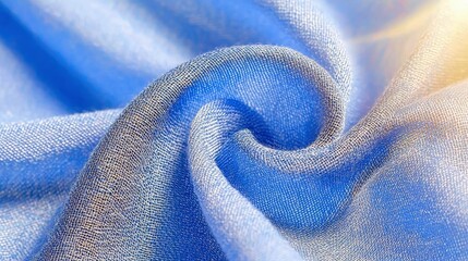 A close-up view of a soft, blue fabric with a textured weave, artfully swirled and illuminated by warm, diffused sunlight from the upper right.
