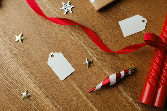 Red ribbon snowflakes stars gift tags and red candles lay on a wooden table surface - Powered by Adobe