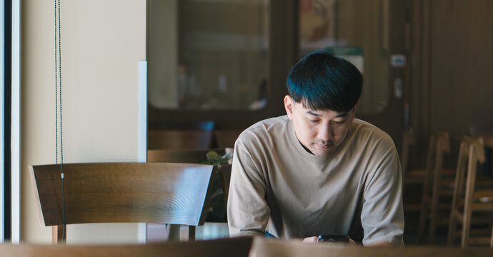 Man looking down at smartphone in coffee shop, symbolizing online lifestyle, social media usage, digital connectivity, and modern communication habit.