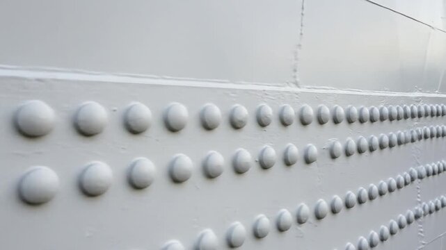 Rows of rivets create a textured pattern on a plain, white metal surface