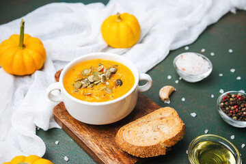 Orange soup with pumpkin seeds and bread on a rustic table with small pumpkins and seasonings.