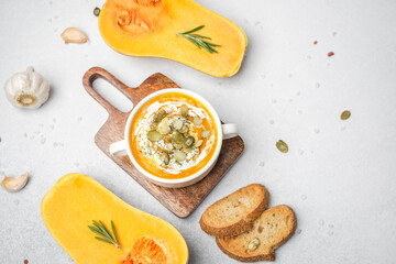 Creamy pumpkin soup with seeds and herbs on a wooden board, served with bread slices and garlic
