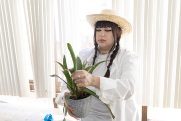 Woman tending green houseplant wearing straw hat