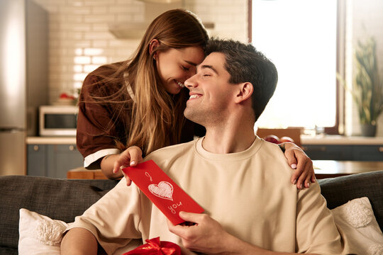 Happy couple celebrating Valentine's Day at home with card and heart-shaped gift box