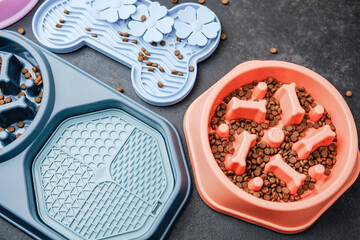 Three colorful pet bowls filled with kibble on a dark textured surface