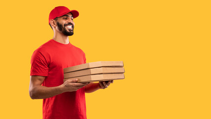 A delivery person smiles while holding multiple pizza boxes against a vibrant yellow background. The individual wears a red shirt and matching cap, showcasing a lively delivery moment.