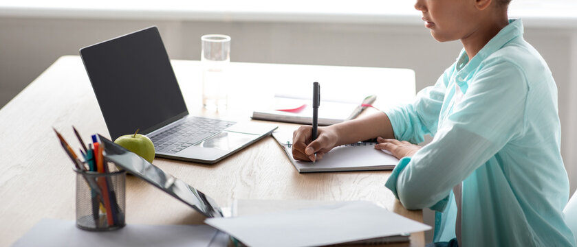 A focused teenage afro american girl student is studying at home using a laptop. She is preparing for tests while writing in her notebook. The environment is calm and conducive to learning. - Powered by Adobe