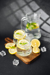 Citrus lemonade with fresh mint leaves and ice cubes in glass jug on bright table in sunny summer kitchen