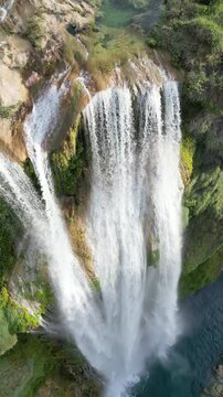 Aerial drone view of Tamul Waterfall cascading down green cliffs into a turquoise pool below. Vertical