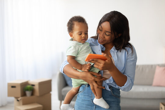 An African American mother holds her baby while showing pictures on a smartphone. They both enjoy viewing cartoons or video calling family members.
