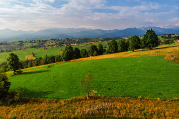 Obraz premium Wide aerial drone panorama of the Tatra Mountains and the village of Sierockie in the Polish Podhale region. Lush green farmlands and rolling hills under a dramatic sky.