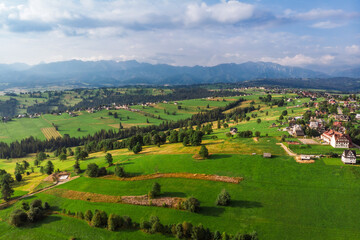Obraz premium Wide aerial panorama of Sierockie village in the Podhale region, Poland. Lush green farmlands and rolling hills with the majestic Tatra Mountains in the distance.