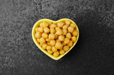Heart shaped bowl of chickpeas on black background for vegan protein, clean eating or food styling concept