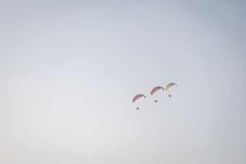 Brightly colored paramotors fly in tight groups across a clear, calm sky during a daytime adventure.