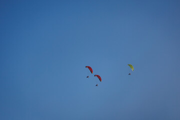 Brightly colored paramotors fly in tight groups across a clear, calm sky during a daytime adventure.