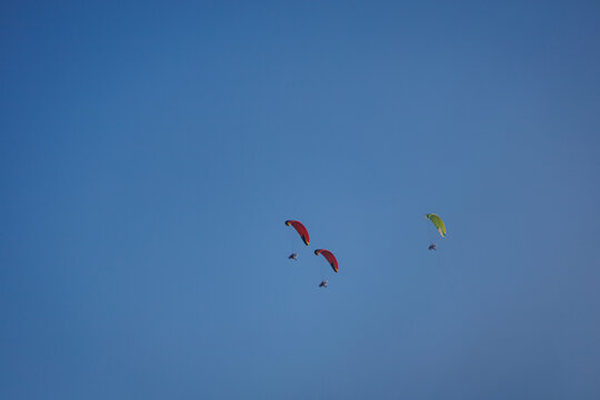 Brightly colored paramotors fly in tight groups across a clear, calm sky during a daytime adventure.
