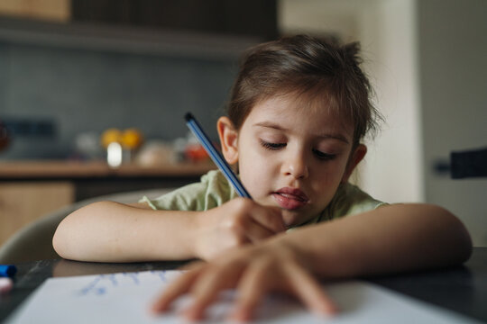 child creating art, young girl concentrating on artwork in cozy kitchen setting with warm light