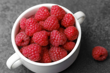 Raspberries in cup on black textured background for gourmet snack or modern food styling concept