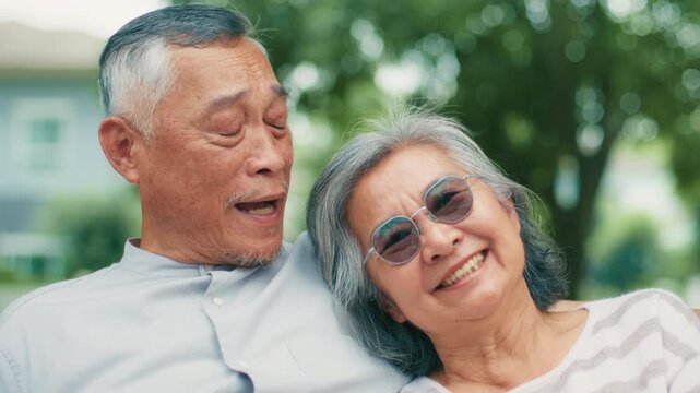 Happy Asian Senior Couple lifestyle retirement relaxing outdoor. Elderly Couple resting on bench in park. Smile enjoying g Mature man and woman enjoying, retirement, quality time together in park.