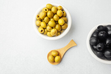 Closeup green and black olives in bowls with wooden spoon on white background