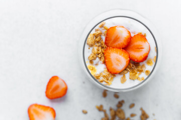 Top view of strawberry yogurt parfait with granola on white
