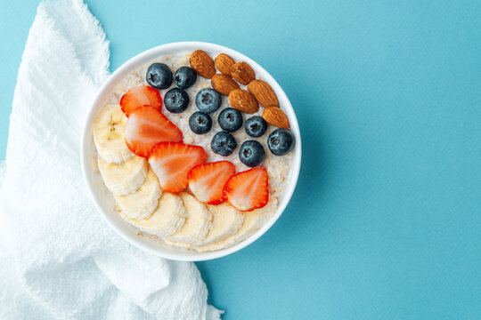 Colorful oatmeal breakfast bowl with fruits and almonds on blue background
