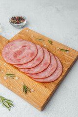 Round sliced sausage on wooden board with rosemary and salt on white background
