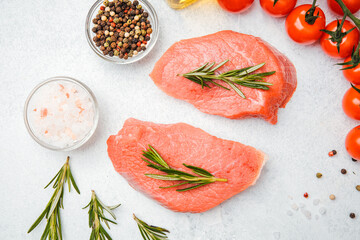 Top view of veal steaks with spices and herbs on white background including close-up of oil and pepper
