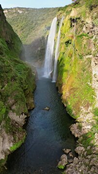 Aerial drone view of Tamul Waterfall cascading down green cliffs into a turquoise pool below. Vertical