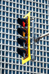 A close-up view of a traffic light in downtown Montreal, captured against the geometric facade of a modern high-rise building, highlighting the vibrant yellow frame and illuminated signals