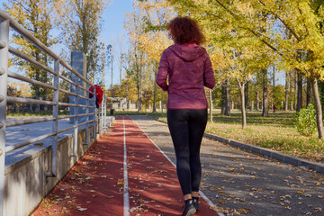 Middle-aged woman in the park running on a running track on a sunny autumn day