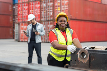 Female dock worker operating equipment at cargo container yard, Confident female laborer working at freight yard with supervisor in background