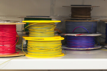 a close-up view of various spools of electrical wire in bright colors, including green, red, yellow, and orange. The reels are arranged on a workbench in a workshop environment, creating a technical a