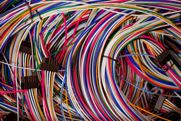 a close-up view of various spools of electrical wire in bright colors, including green, red, yellow, and orange. The reels are arranged on a workbench in a workshop environment, creating a technical a