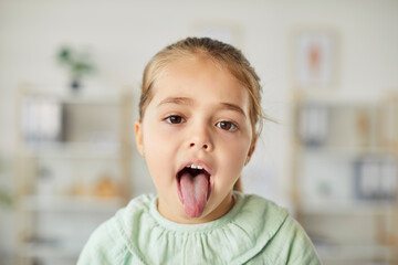 Portrait of a girl patient showing tongue for a dental or throat inspection during a healthcare...