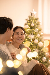 Winter lovers' date: A couple smiling together before the Christmas tree Warm, happy moments under indoor illuminations