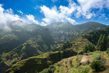 Naklejka premium Scenic terraced mountains of Santo Antão, Cape Verde, with lush green slopes, dramatic valleys and a bright sky, captured in natural sunlight