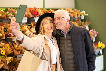 Senior couple smiling, capturing a moment together using a smartphone in a flower shop